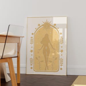 May include: A framed wall art print featuring a gold-toned illustration of a human silhouette centered within an arched frame. The design includes a sun motif at the top, surrounded by small stars, floral elements, and leafy branches on both sides.