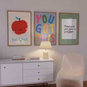 May include: Three framed art prints with positive messages. One features a red apple with the words "Be kind." Another says "YOU GOT THIS" in colorful letters. The third says "Please write your name on your paper."