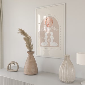 K&ouml;nnte beinhalten: Ein gerahmter Druck mit einem minimalistischen Design, das zwei Figuren in kniender Haltung zeigt, die sich gegen&uuml;berstehen. Die Figuren sind wei&szlig; vor einem pfirsichfarbenen Hintergrund mit einem gro&szlig;en orangen Kreis und floralen Akzenten. Der Druck ist in Wei&szlig; gerahmt.