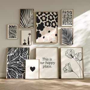 May include: A selection of framed art prints with botanical and abstract designs. The prints feature black and white patterns, floral motifs, and the text "This is our happy place." The frames have a natural wood finish.