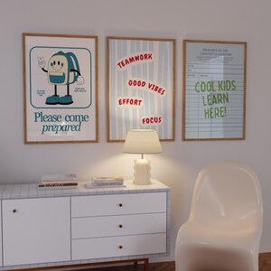 May include: Three framed posters with motivational messages hang on a white wall. One poster features a cartoon backpack and the text "Please come prepared." Another says "Teamwork, Good Vibes, Effort, Focus." The third reads "Cool Kids Learn Here!"