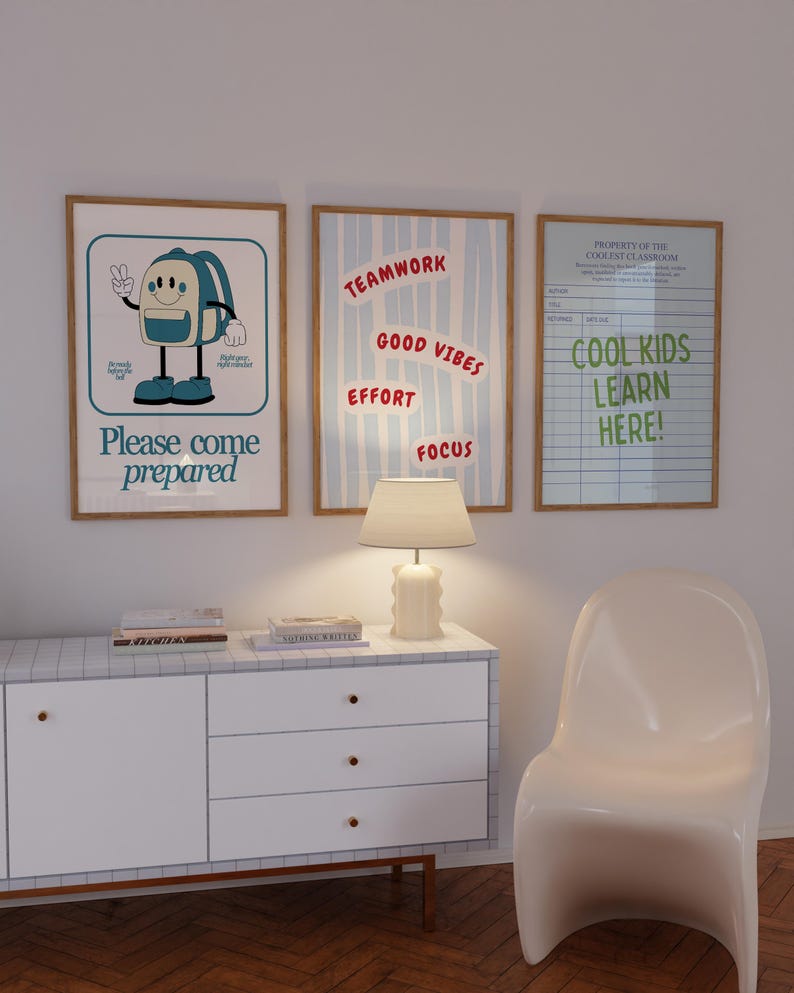 May include: Three framed posters with motivational messages hang on a white wall. One poster features a cartoon backpack and the text "Please come prepared." Another says "Teamwork, Good Vibes, Effort, Focus." The third reads "Cool Kids Learn Here!"