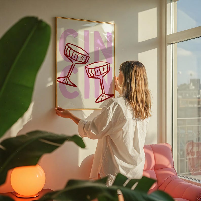 Puede incluir: Una impresi&oacute;n art&iacute;stica enmarcada con la palabra "GIN" en letras rosas y dos copas de c&oacute;ctel rojas. La impresi&oacute;n est&aacute; en un marco dorado y se cuelga en una pared blanca.