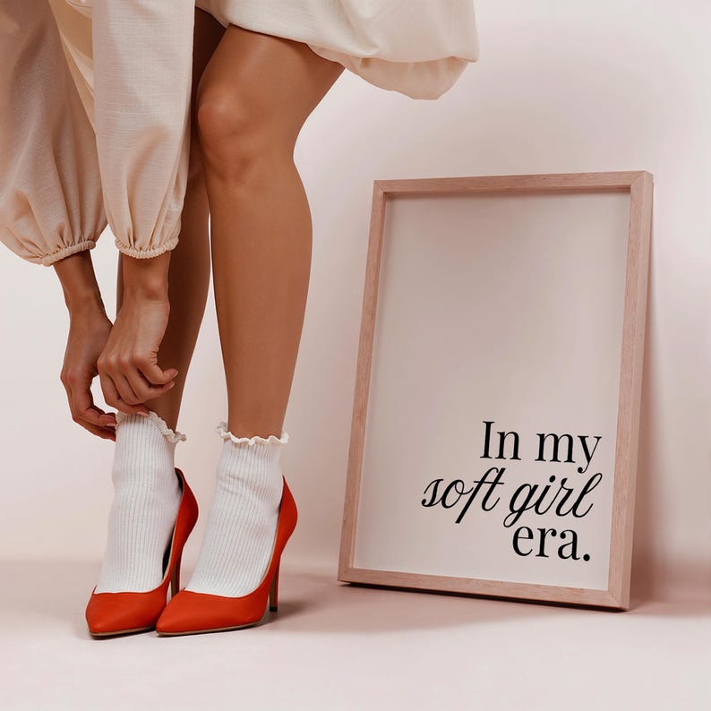Puede incluir: Un par de tacones altos naranjas con calcetines blancos acanalados y una impresi&oacute;n enmarcada. La impresi&oacute;n dice "In my soft girl era." Los tacones tienen una punta puntiaguda y un tac&oacute;n de aguja. Los calcetines tienen un borde con volantes.