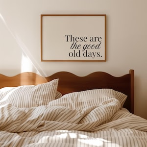 以下が含まれることがあります： 「These are the good old days」のテキストが入った額入りのプリント。寝室の様子。フレームは茶色で、テキストは黒。ベッドにはストライプの寝具と木製のヘッドボードがあります。