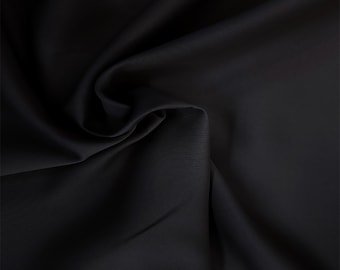 May include: A close-up of a smooth, black fabric with a subtle sheen. The fabric is draped and folded, creating soft curves and folds.