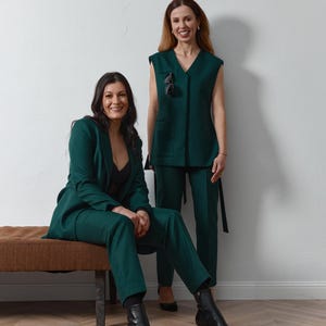 Peut inclure: Deux personnes portant des costumes vert foncé assortis. L'une est assise dans un costume avec un blazer et un pantalon, l'autre porte un gilet et un pantalon. Les deux tenues sont élégantes et professionnelles, avec des bottes et des talons noirs.
