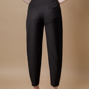 May include: Black high-waisted pants with a wide leg silhouette. The pants have a front zipper and button closure, and two back pockets.
