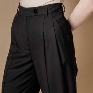 May include: Black high-waisted pants with pleats and a button closure.