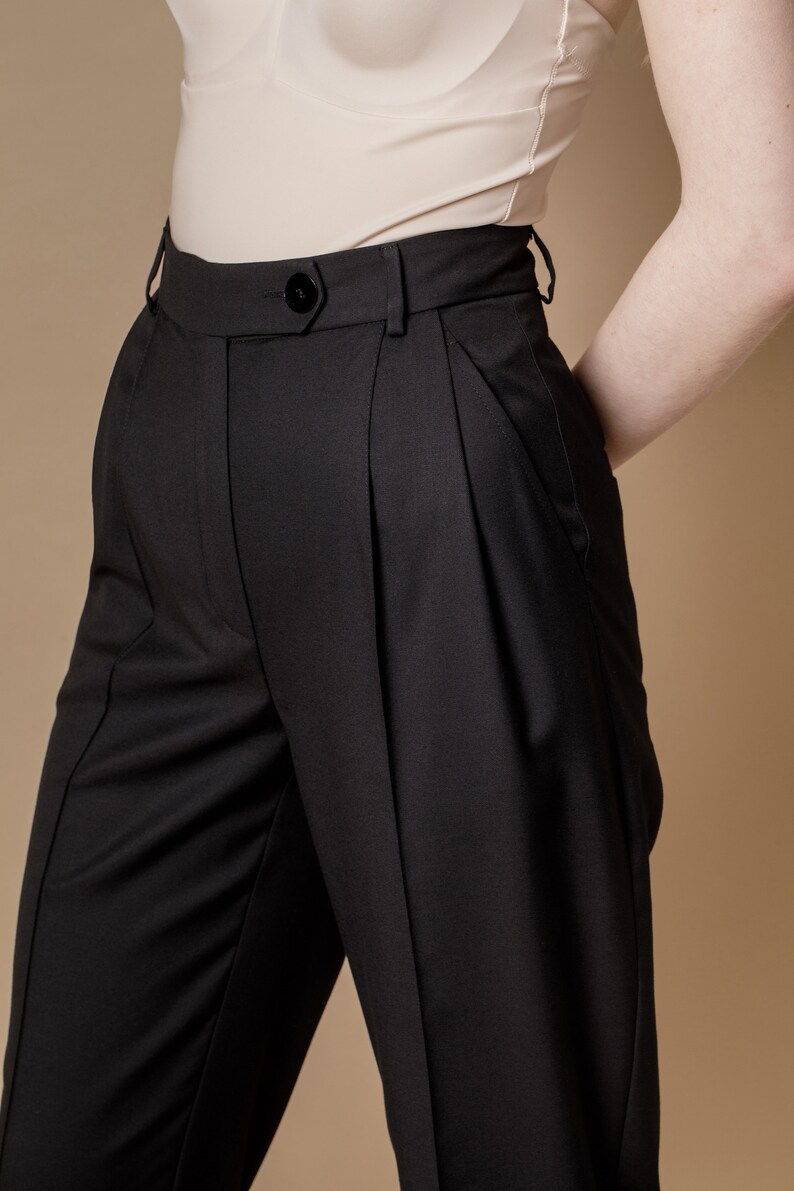 May include: Black high-waisted pants with pleats and a button closure.