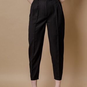 May include: Black high-waisted pants with pleats and a button closure. The pants are cropped and have a straight leg.