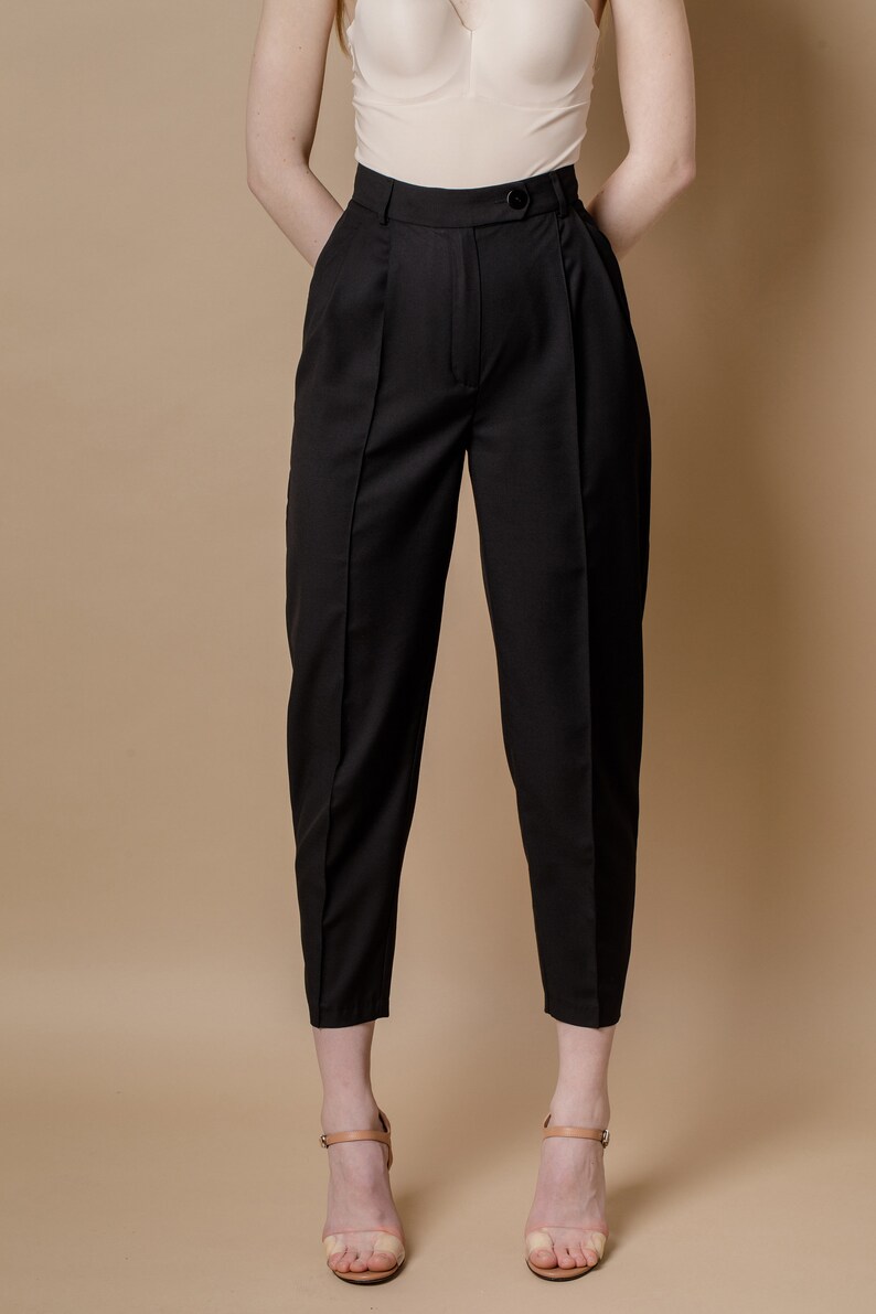 May include: Black high-waisted pants with pleats and a button closure. The pants are cropped and have a straight leg.