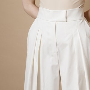 Palazzo pants for women with front pleats, high waist and side pockets. Trousers are made from white cotton fabric with zipper and hook-and-eye closure