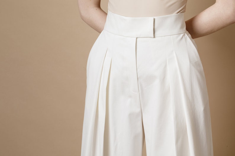 Palazzo pants for women with front pleats, high waist and side pockets. Trousers are made from white cotton fabric with zipper and hook-and-eye closure