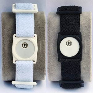 May include: Two wristbands with adjustable straps and a white square face with a black circle in the centre. The wristband on the left is white and the wristband on the right is black.