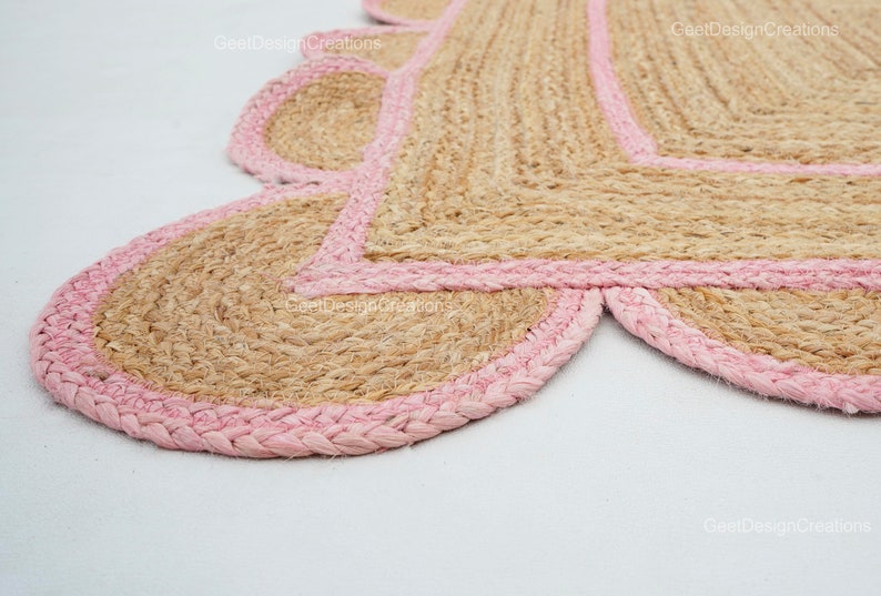 May include: A pink and beige jute rug with a scalloped edge. The rug is made of natural fibers and has a rustic, handmade look.