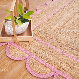 May include: A natural fiber rug with a pink border and scalloped edges. The rug is made of jute and has a natural, earthy look.