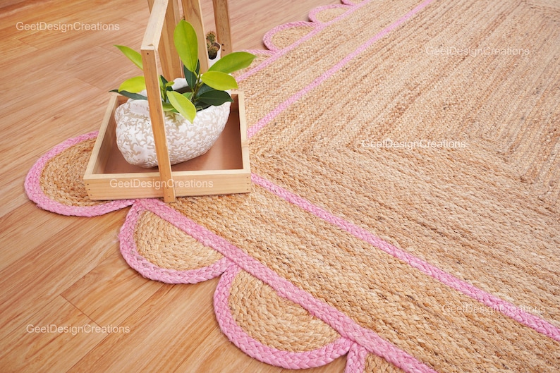 May include: A natural fiber rug with a pink border and scalloped edges. The rug is made of jute and has a natural, earthy look.