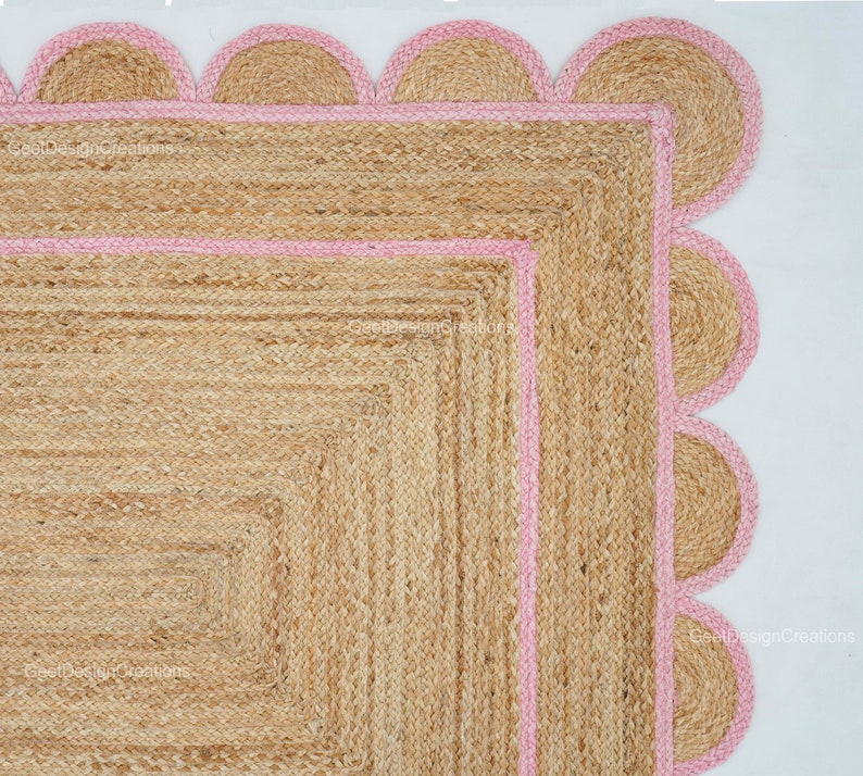 May include: A square jute rug with a pink scalloped border. The rug has a woven texture and is made of natural fibers.