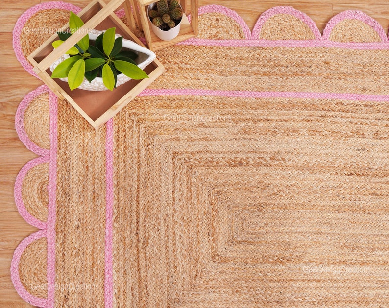 May include: A natural fiber rug with a pink border. The rug has a scalloped edge and is made of jute.