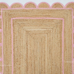 May include: A natural fiber rug with a pink scalloped border. The rug is made of jute and has a woven texture.