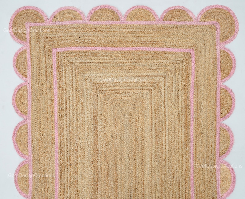 May include: A natural fiber rug with a pink scalloped border. The rug is made of jute and has a woven texture.