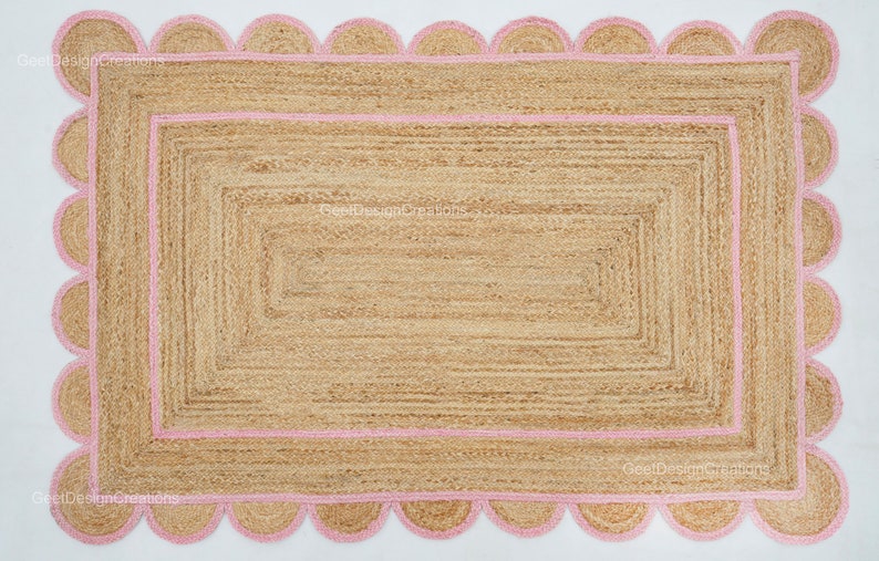 May include: A natural fiber rug with a pink scalloped border and a woven design. The rug has a rectangular shape and is made of jute.