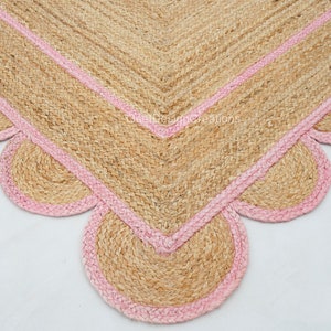 May include: A natural fiber rug with a pink border and scalloped edges. The rug is made of jute and has a natural, earthy look.