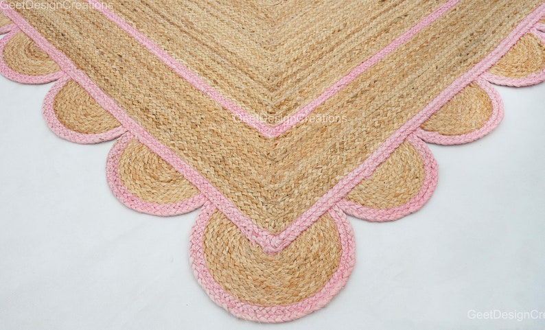 May include: A natural fiber rug with a pink border and scalloped edges. The rug is made of jute and has a natural, earthy look.