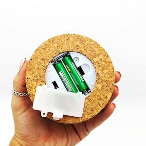May include: A round light with a cork covering, a white plastic battery compartment and two green AA batteries inside.