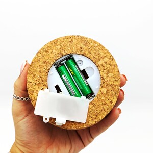 Peut inclure: Une lumi&egrave;re ronde recouverte de li&egrave;ge avec un compartiment &agrave; piles en plastique blanc et deux piles AA vertes &agrave; l'int&eacute;rieur.