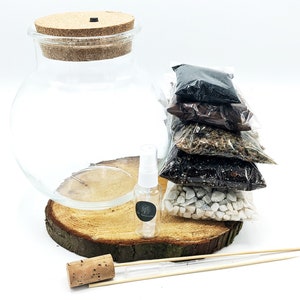 Peut inclure: Un kit de terrarium avec un bocal en verre transparent, un couvercle en li&egrave;ge, une base en bois et cinq petits sachets de mat&eacute;riaux de diff&eacute;rentes couleurs. Le kit comprend &eacute;galement un petit vaporisateur et un b&acirc;tonnet en bois.