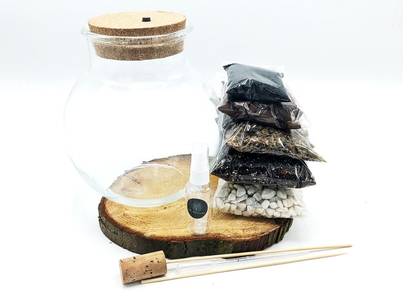 Peut inclure: Un kit de terrarium avec un bocal en verre transparent, un couvercle en li&egrave;ge, une base en bois et cinq petits sachets de mat&eacute;riaux de diff&eacute;rentes couleurs. Le kit comprend &eacute;galement un petit vaporisateur et un b&acirc;tonnet en bois.