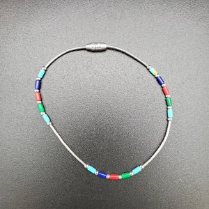 May include: A silver chain necklace with colorful rectangular beads. The beads are red, blue, green, and turquoise.