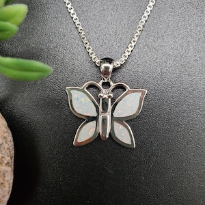 May include: A silver chain necklace with a butterfly pendant made of white opal. The butterfly has a silver outline and a black body.