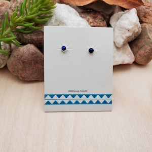 Op de afbeelding: Een paar oorbellen met een sterling zilveren oorbel met kleine, ronde, donkerblauwe edelstenen. De oorbellen worden getoond op een witte kaart met de tekst "Sterling Silver" erop gedrukt.