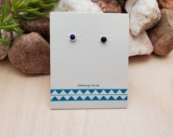 May include: A pair of sterling silver stud earrings with small, round, dark blue gemstones. The earrings are displayed on a white card with the text "Sterling Silver" printed on it.
