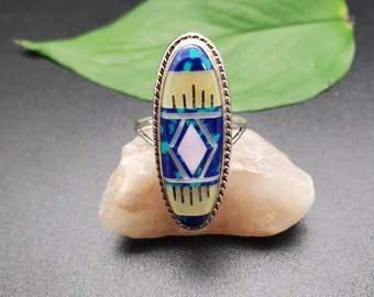 Op de afbeelding: Ovale ring met een zilveren band en een kleurrijk inlay-ontwerp. De inlay heeft een geometrisch patroon met blauwe, groene, witte en roze stenen.