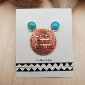 May include: A pair of sterling silver earrings with turquoise stones, shown next to a US penny for size comparison.  Sterling Silver.