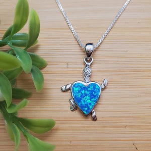 May include: A silver necklace with a blue opal heart-shaped turtle pendant.