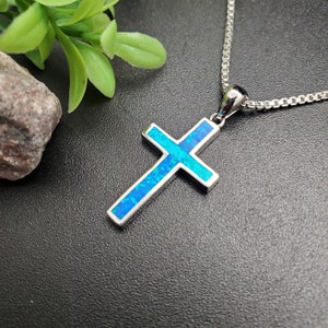 May include: A silver chain necklace with a blue opal cross pendant. The cross is a simple design with a smooth, polished finish.