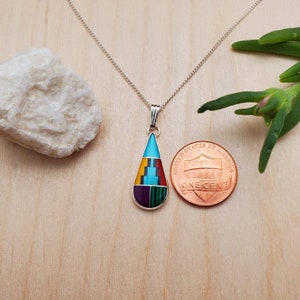 Puede incluir: Un collar de cadena de plata con un colgante en forma de l&aacute;grima. El colgante est&aacute; hecho de turquesa, rojo, amarillo, verde y morado. El colgante es aproximadamente del tama&ntilde;o de una moneda de un centavo de euro.