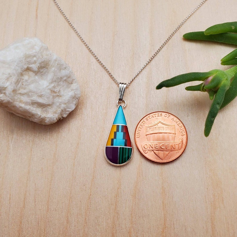 Puede incluir: Un collar de cadena de plata con un colgante en forma de l&aacute;grima. El colgante est&aacute; hecho de turquesa, rojo, amarillo, verde y morado. El colgante es aproximadamente del tama&ntilde;o de una moneda de un centavo de euro.