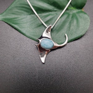 Puede incluir: Un collar con un colgante de plata con forma de manta raya con una piedra preciosa azul en el centro.