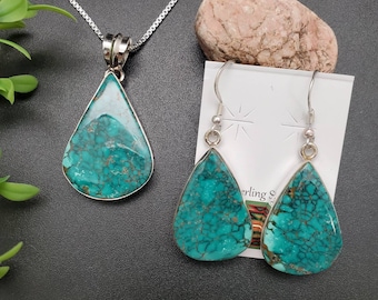 May include: A turquoise and silver teardrop pendant necklace and matching earrings set. The turquoise stones have a unique, marbled pattern.