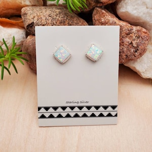 May include: A pair of sterling silver earrings with white opal square stones. The earrings are displayed on a white card with the text "Sterling Silver".
