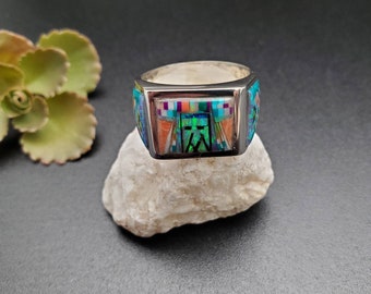 May include: A silver ring with a colorful inlay design. The inlay features geometric shapes and patterns in shades of blue, green, orange, and white.