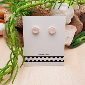 May include: A pair of sterling silver stud earrings with pink rose quartz stones. The earrings are displayed on a white card with black and white geometric pattern and the text "Sterling Silver".
