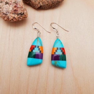 May include: A pair of dangle earrings with turquoise, purple, green, orange, and black inlay. The earrings have silver hooks.