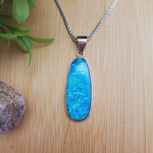 May include: A silver chain necklace with a teardrop-shaped pendant featuring a blue opal gemstone.
